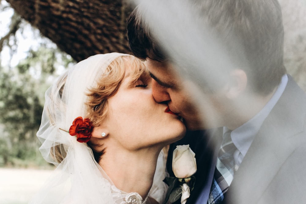 selective focus photo of bride and groom kissing near tree during daytime