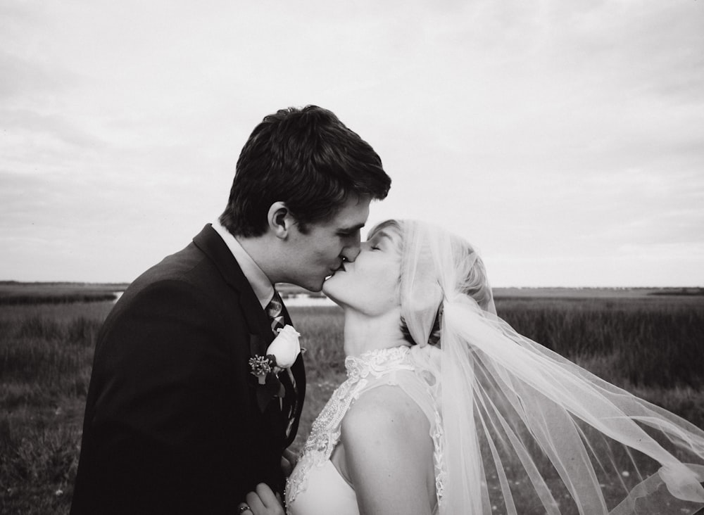grayscale photography of bride and groom kissing surrounded by grass