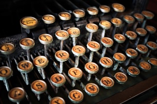 An array of vintage typewriter keys with worn-out, yellowed letters and numbers, mounted on metal stems, set against a dark background.