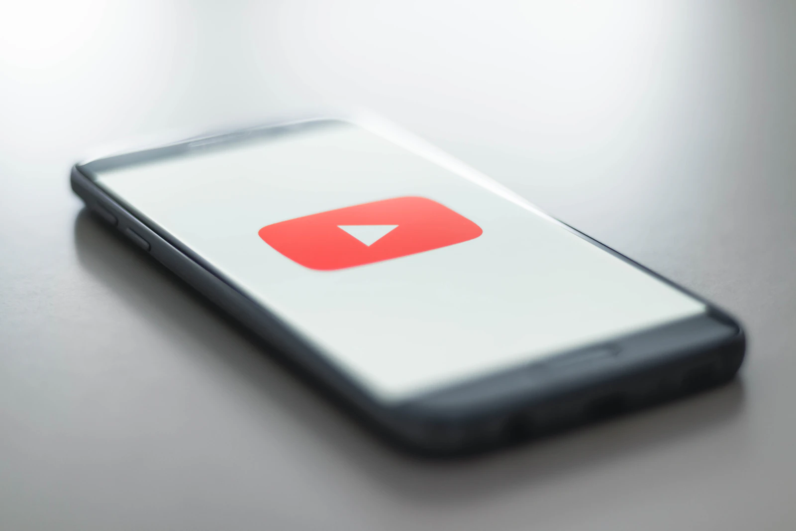 A smartphone lying on a desk showing the YouTube logo on its screen