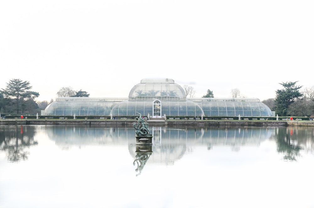 a pond with a statue in front of a glass house