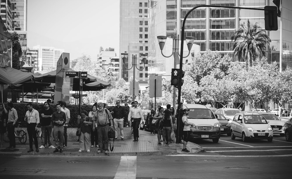 grayscale photo of people walking on sidewalk near buildings