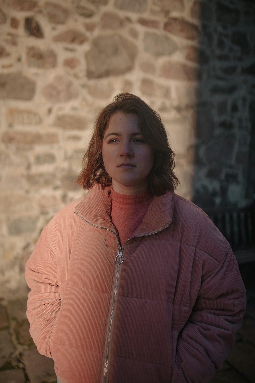 standing woman wearing pink zip-up jacket near bricked wall