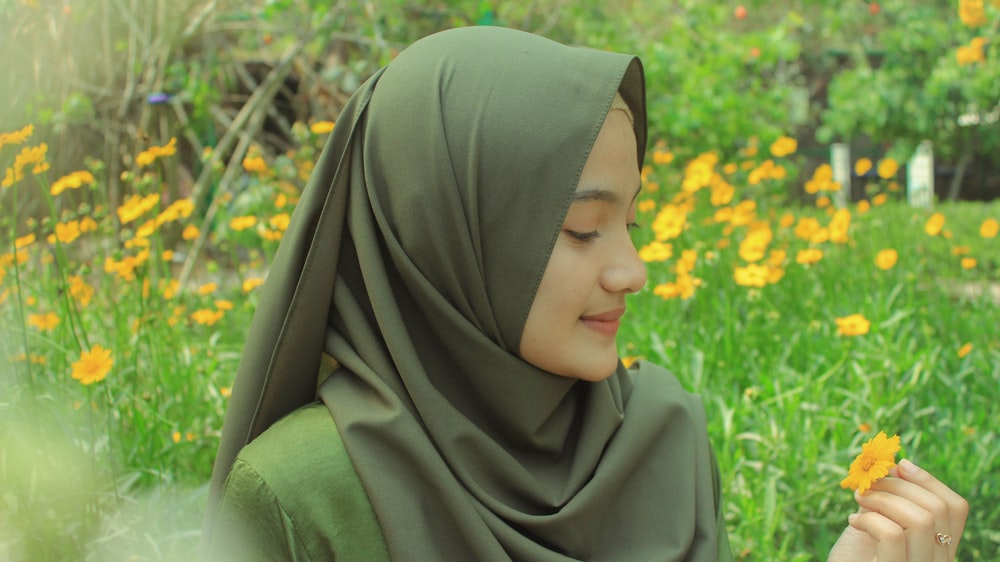 mujer con hiyab gris sosteniendo una flor amarilla