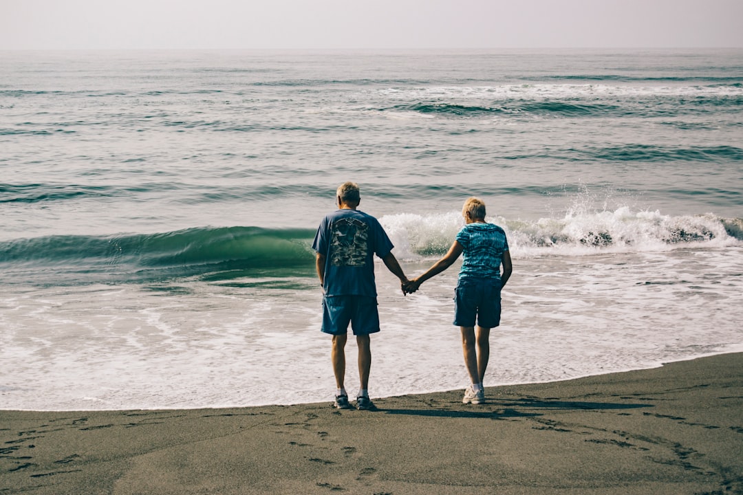 man and woman holding hands together while standing on seashore