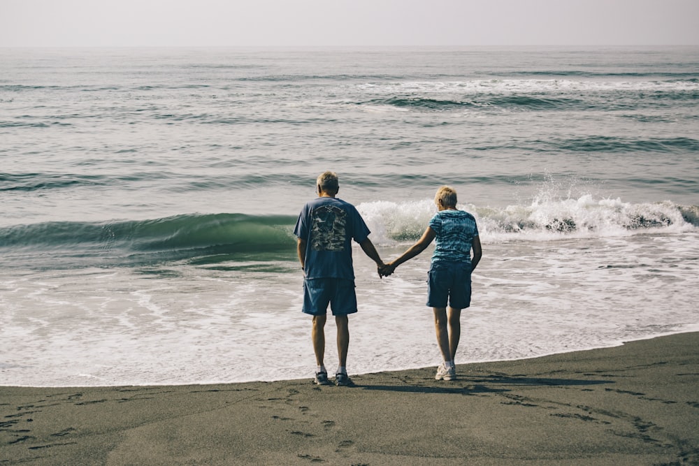 man and woman holding hands together while standing on seashore