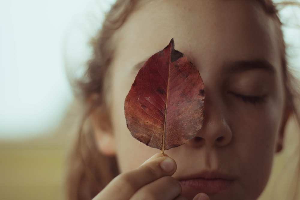 woman covering right eye using leaf