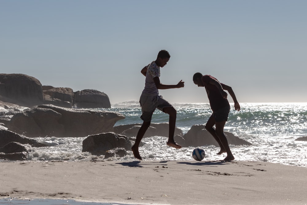 two men playing with soccer ball near seashore