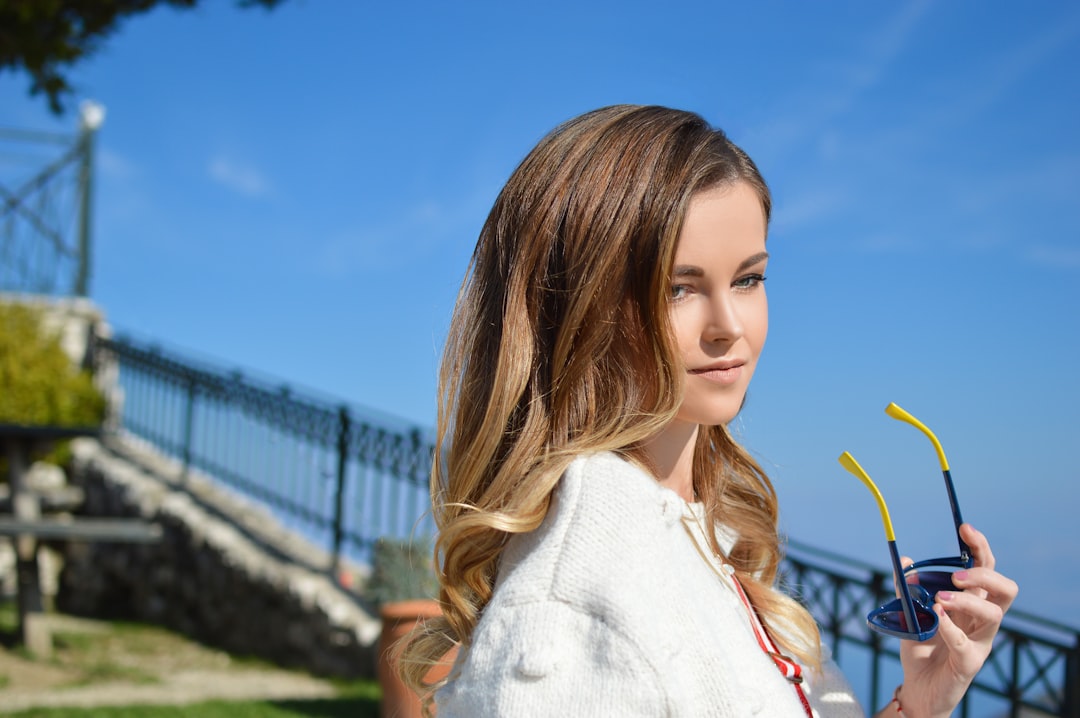 woman in white jacket holding sunglasses