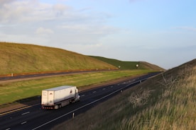 A freight truck driving along a highway surrounded by green fields.