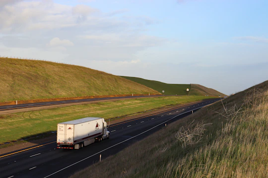 A sleek semi-truck driving along a wide open highway under a clear blue sky.