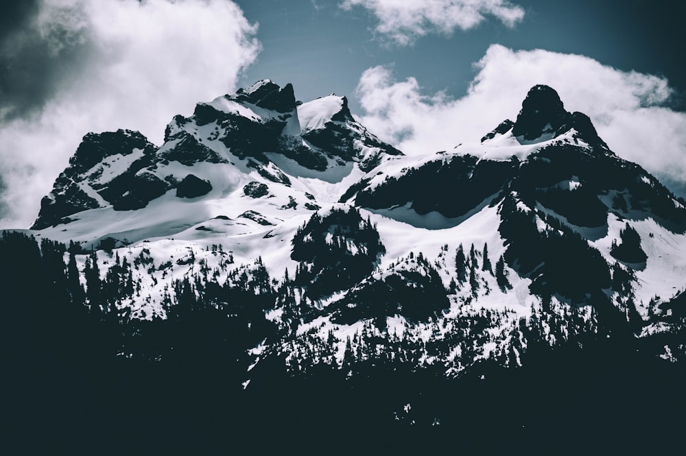 white snow covering rocky mountain under white clouds