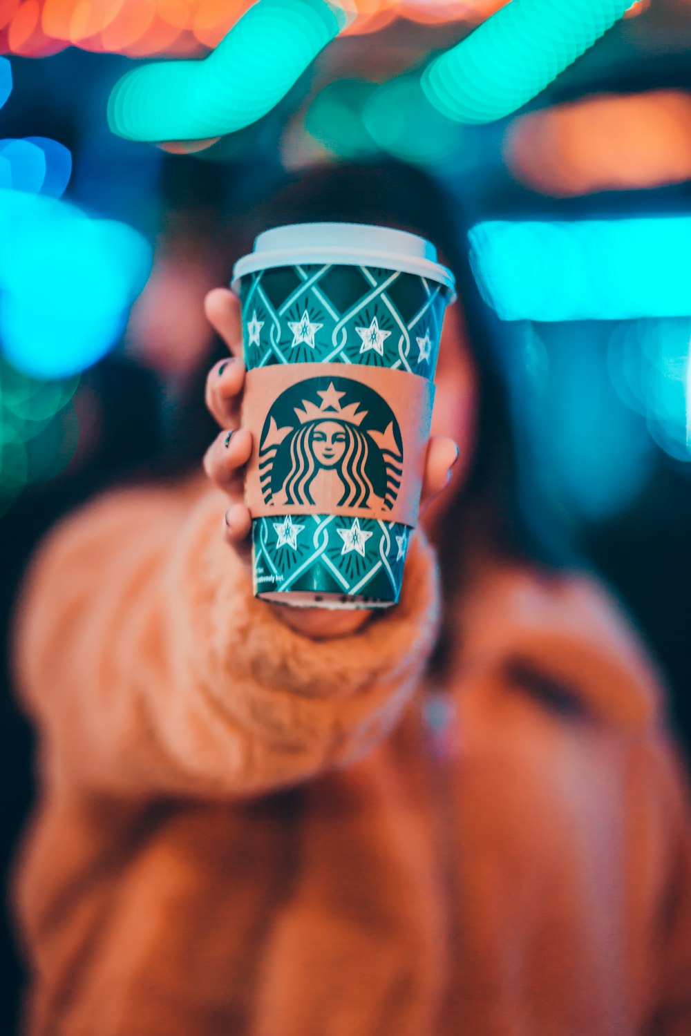 femme sur veste marron montrant une tasse à café Starbucks verte et brune