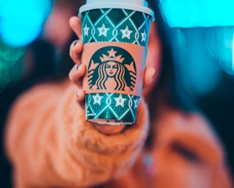 woman on brown jacket showing green and brown Starbucks coffee cup