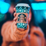 woman on brown jacket showing green and brown Starbucks coffee cup