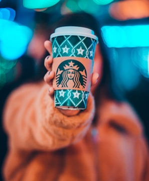 woman on brown jacket showing green and brown Starbucks coffee cup