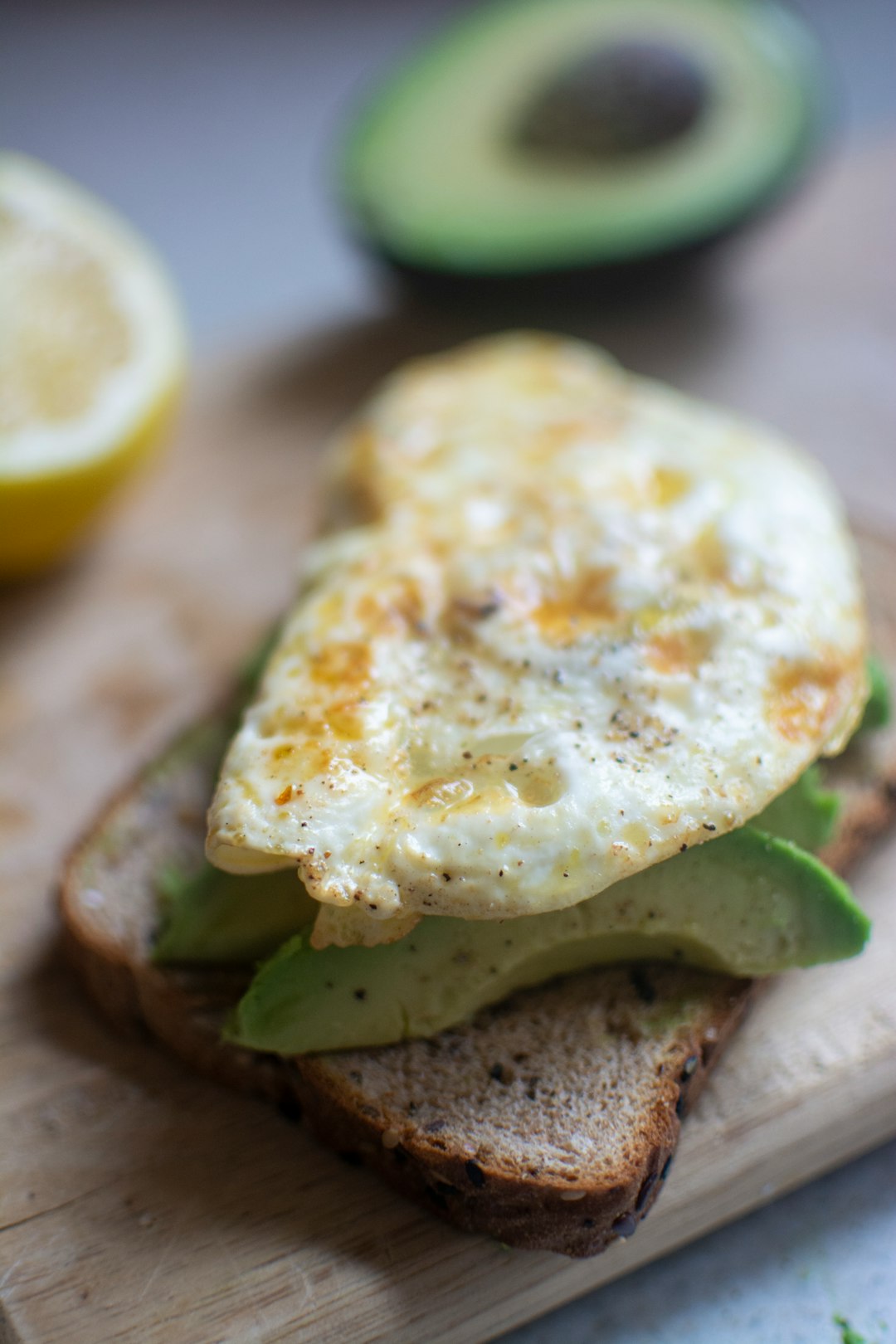 egg on top of avocado and bread on chopping board