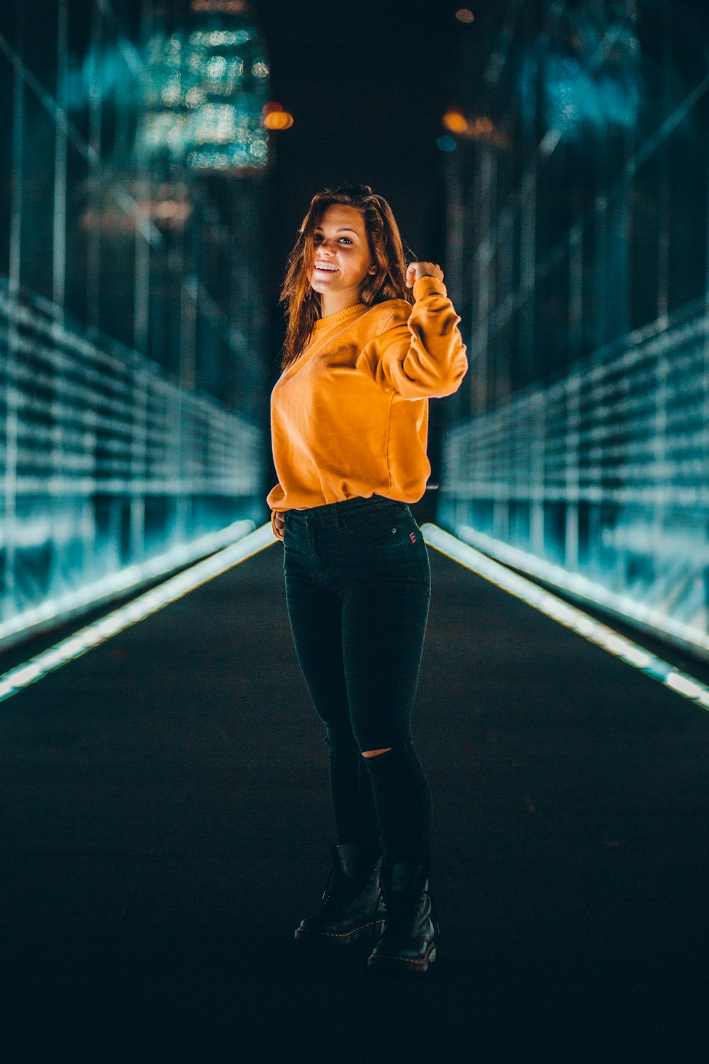 selective focus photography of woman standing wearing orange long-sleeved shirt and distressed black denim jeans