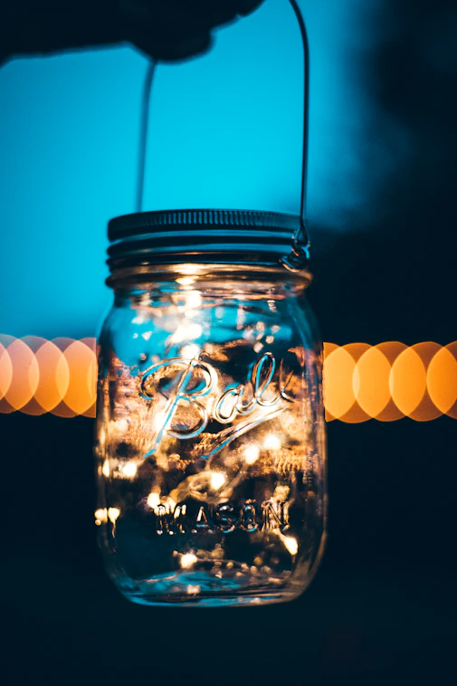A cozy mason jar glowing softly on a rustic wooden table beneath a starry night sky.