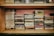 A vintage collection of music cassette tapes is organized on a wooden shelf. The tapes are stacked in groups and feature various artists and bands, each with distinct album covers and titles. The shelf has a rustic appearance with hints of wear and age, adding a nostalgic feel.