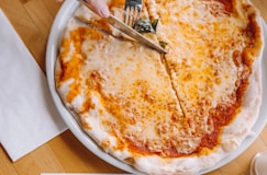 person slicing pizza using knife and fork