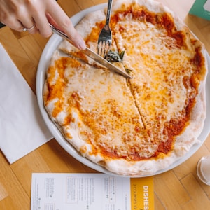 person slicing pizza using knife and fork