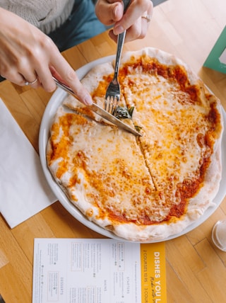 person slicing pizza using knife and fork