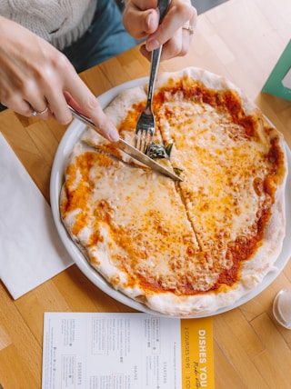 person slicing pizza using knife and fork