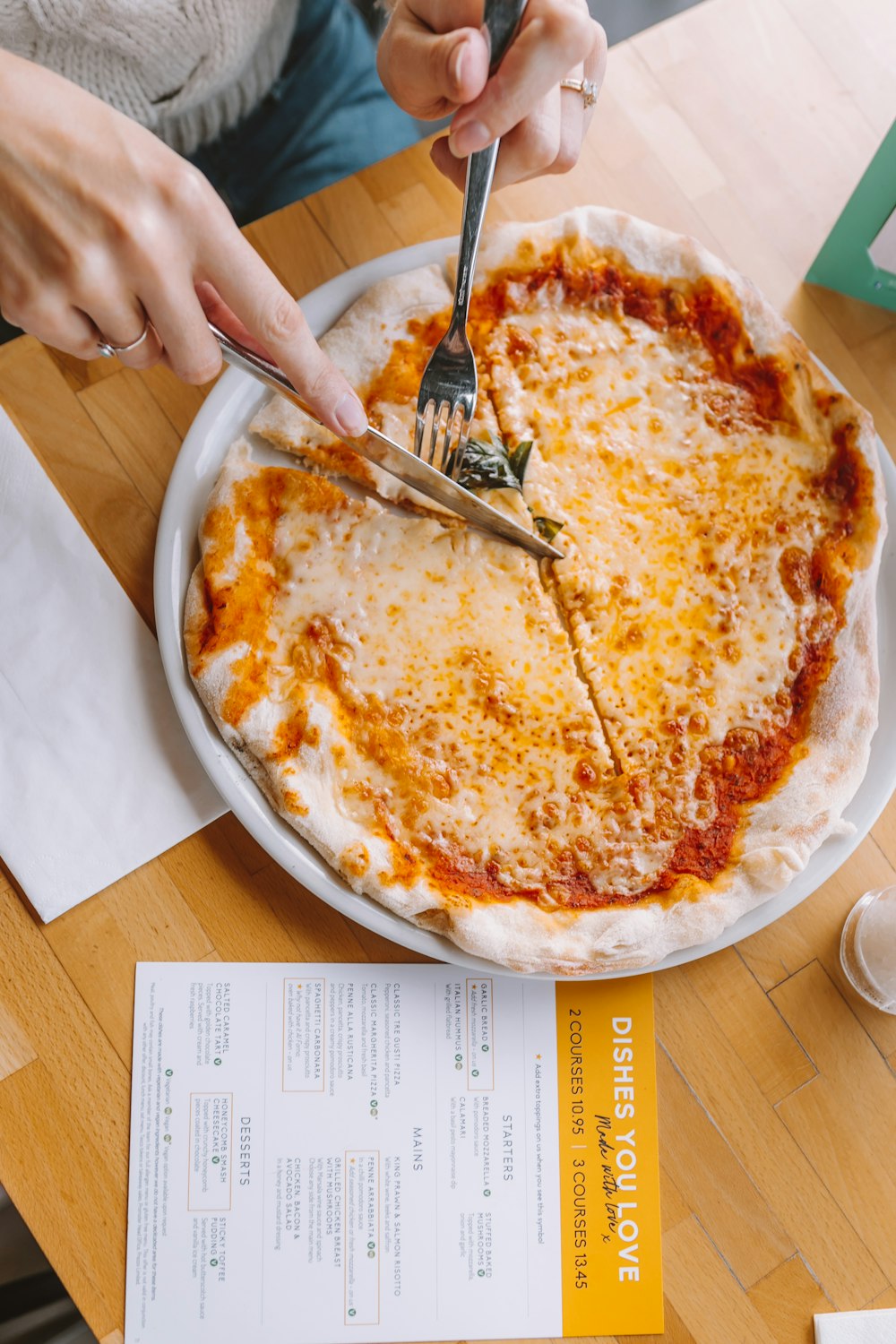 person slicing pizza using knife and fork