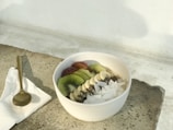 A minimalist bowl of chia pudding with sliced kiwi and coconut flakes on a cream-colored table