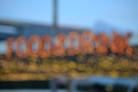 A blurred image with out-of-focus lights forming the words 'FOOD & DRINK' in a bokeh style. The background is soft, with hints of a blue sky and some structural elements possibly from a building.