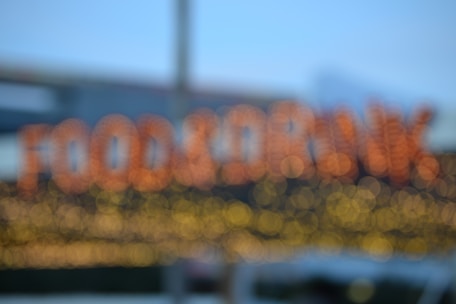A blurred image with out-of-focus lights forming the words 'FOOD & DRINK' in a bokeh style. The background is soft, with hints of a blue sky and some structural elements possibly from a building.