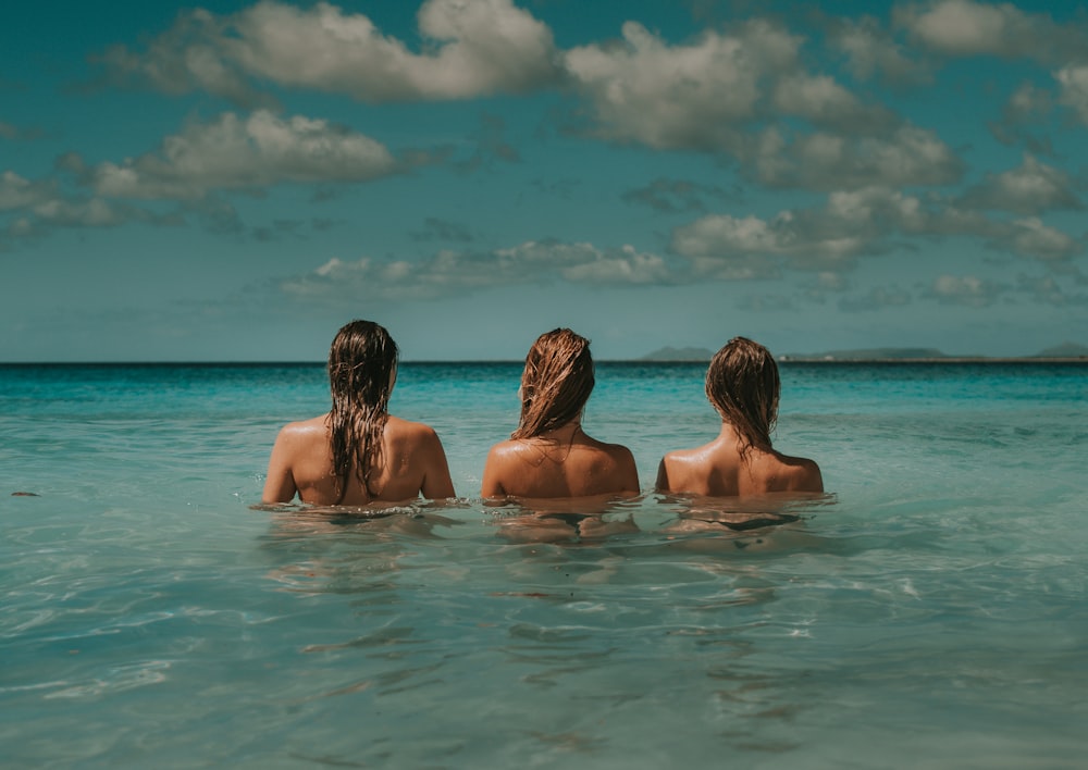 Tres mujeres en el agua mirando el mar bajo nubes blancas