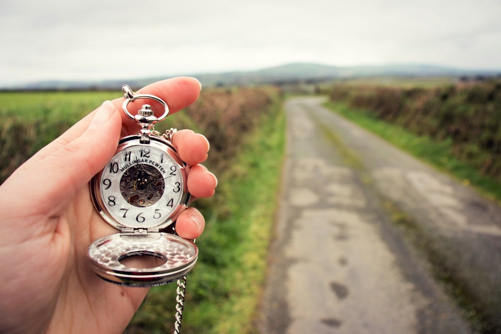 person holding silver-colored pocket watch