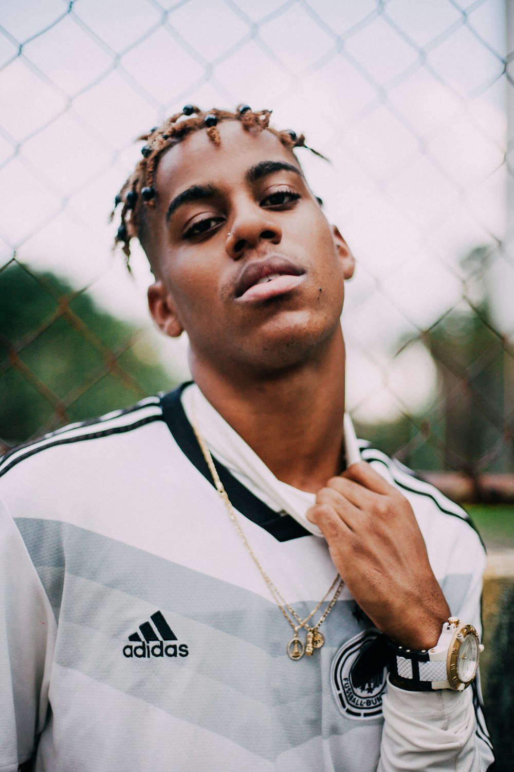 selective focus photography of man wearing adidas Germany soccer jersey shirt beside link fence