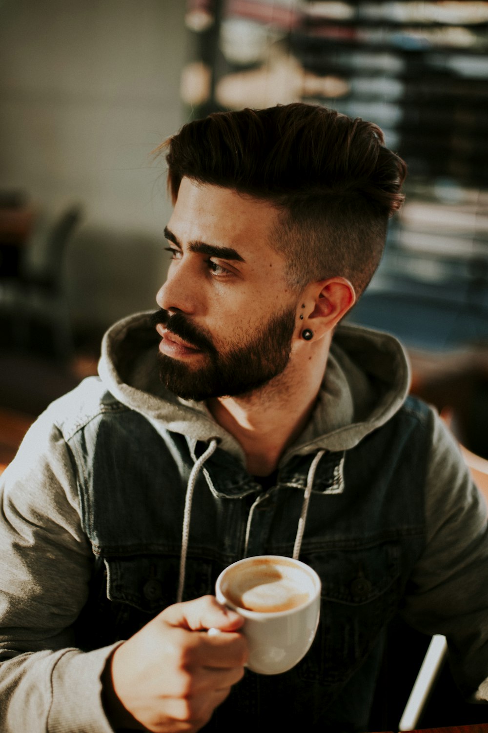 shallow focus photo of man in hoodie holding white ceramic mug