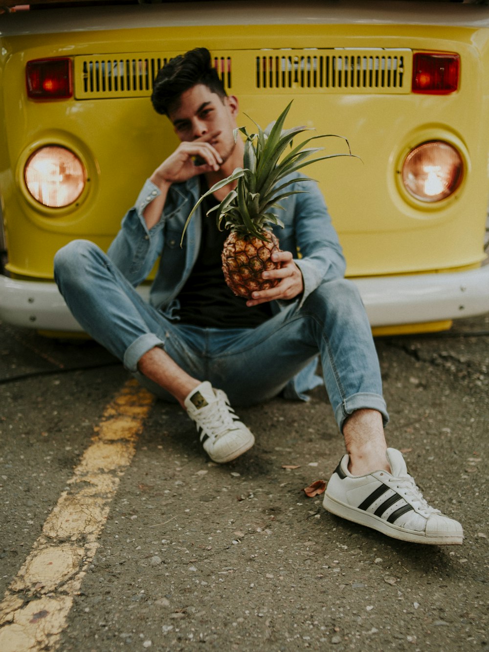 man holding pineapple while leaning on yellow van