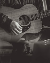 greyscale photography of person playing acoustic guitar