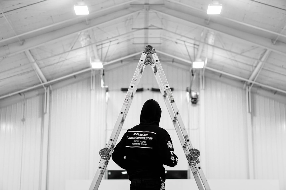 low saturation photography of person in black hooding standing infront of ladder