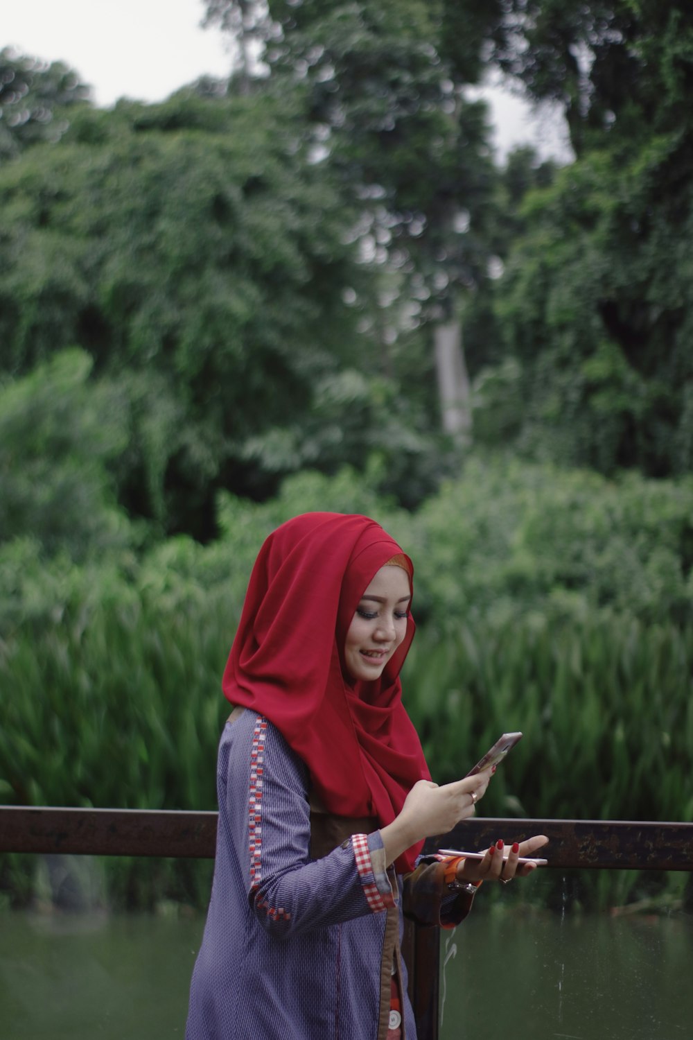 smiling woman while looking at her smartphone near metal railing