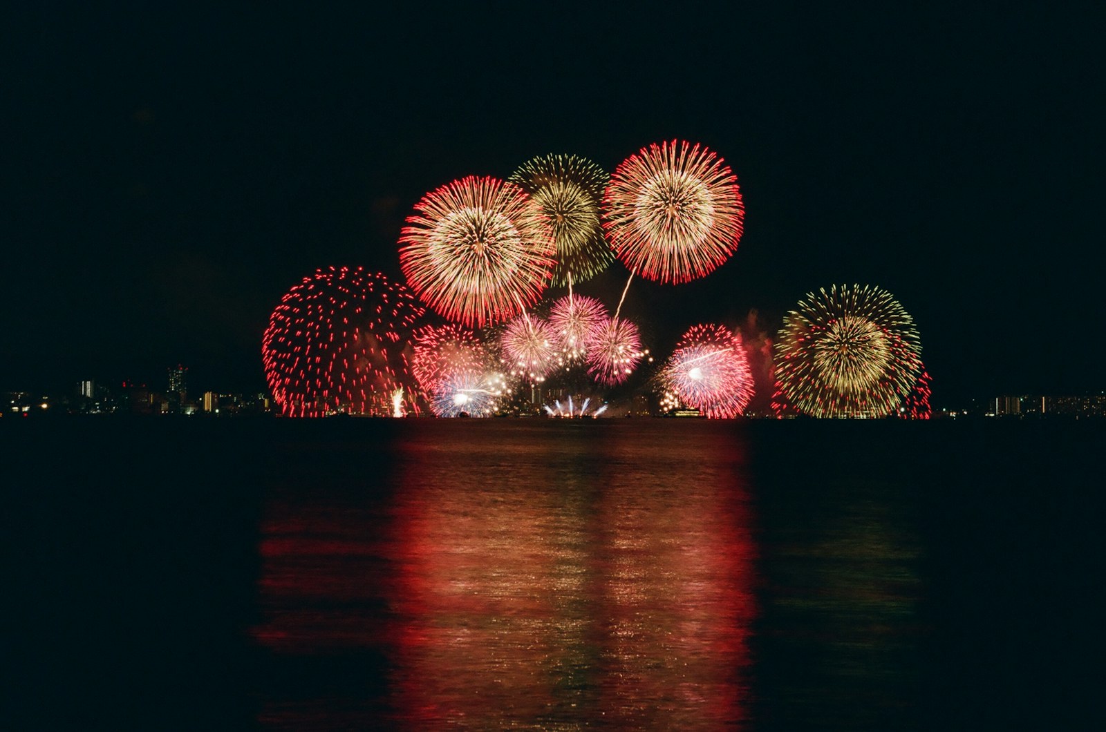 Red and gold fireworks reflected on dark water at night