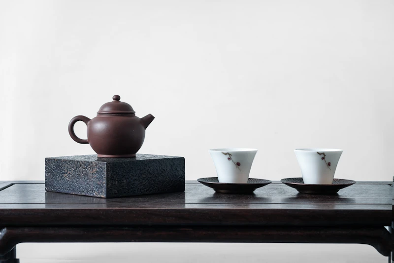 A brown iron teapot with cups on a dark surface