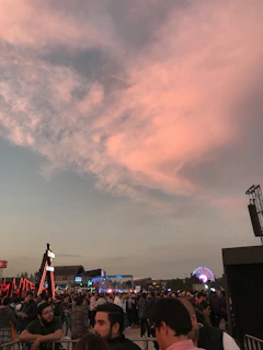 A lively crowd at a sunset outdoor event with colorful lights.