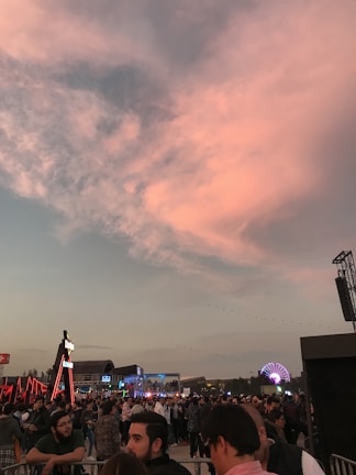 An aerial panorama of a large outdoor event with crowds and stages, captured during golden hour.