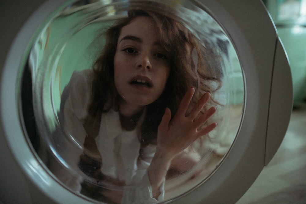 woman in white shirt looking through washing machine glass door
