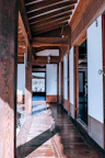 Sunlit corridor leading to guest rooms with traditional wooden doors and potted plants.