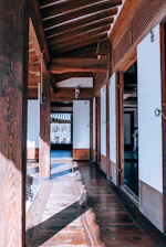Sunlit corridor leading to guest rooms with traditional wooden doors and potted plants.