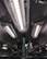 A series of industrial fluorescent lights are encased in protective grids, mounted on a dark ceiling with visible pipes and mechanical components.
