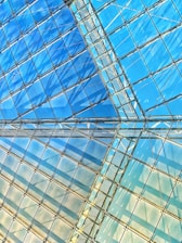Abstract view of a geometric glass ceiling structure reflecting the sky, with intersecting lines and shadows creating a dynamic pattern.
