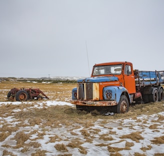 blue and orange stake truck on field near brown farm tractor